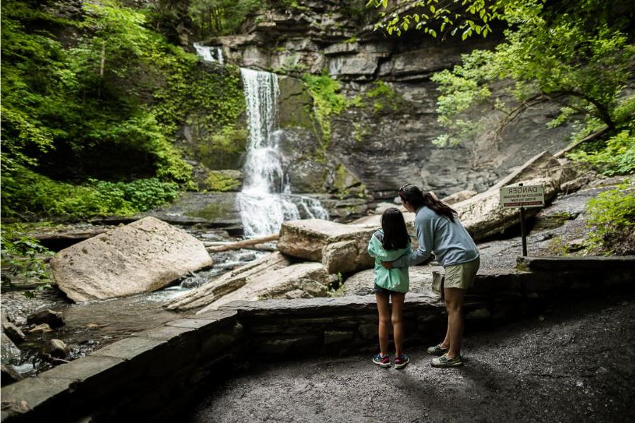 A mother and young daughter outside looking at a waterfall in the fall at Fillmore Glen State Park